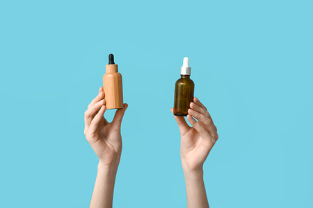 Female hands with bottles of cosmetic products on blue backgroundの写真素材