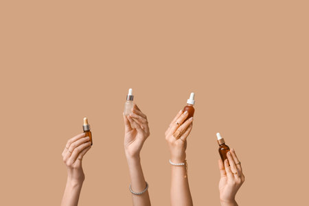 Female hands holding different bottles of cosmetic products on beige backgroundの写真素材