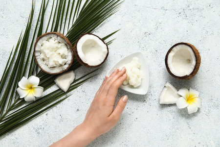 Female hand, palm leaf, flowers and bowl of natural coconut oil on grunge backgroundの写真素材