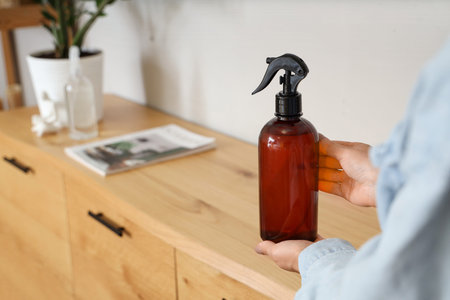 Woman with bottle of aroma spray at home, closeup