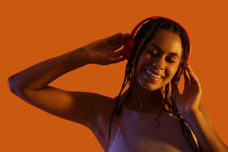 Young African-American woman listening to music on color background