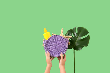 Female hands with bag, sunscreen cream, starfish and monstera leaf on green background. Travel conceptの写真素材