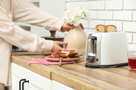 Man with white toaster, bread slices and strawberries on wooden table in kitchenの写真素材