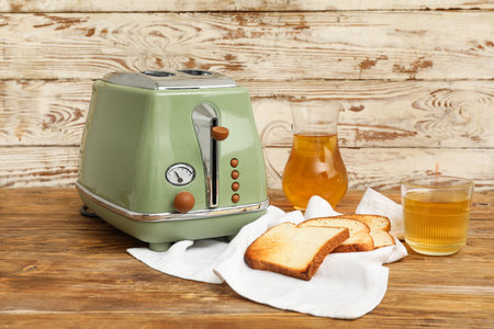 Green toaster with bread slices, jug and glass of juice on wooden background