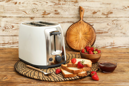 White toaster with bread slices, strawberries and jam on wooden background