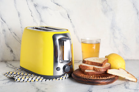 Yellow toaster with bread slices, lemon and glass of juice on white marble backgroundの写真素材