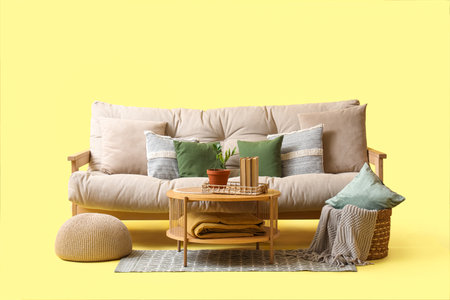 Comfortable white sofa and wooden coffee table with books on yellow backgroundの写真素材