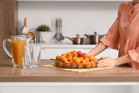 Young woman with tray full of apricots and jug of juice in kitchenの写真素材