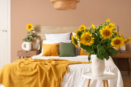 Stylish bedroom with big bed and vases of sunflowers bouquets on stoolの写真素材