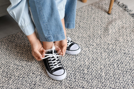 Woman in black sneakers and jeans tying shoe lace at home