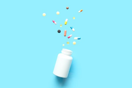 Bottle with different flying pills on blue background. Top view