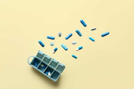 Plastic container with flying blue pills on yellow background. Top viewの写真素材