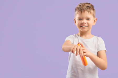 Cute little boy applying sunscreen on lilac backgroundの写真素材