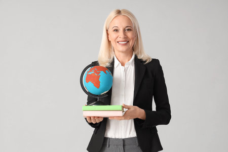 Female Geography teacher with globe and books on light backgroundの写真素材
