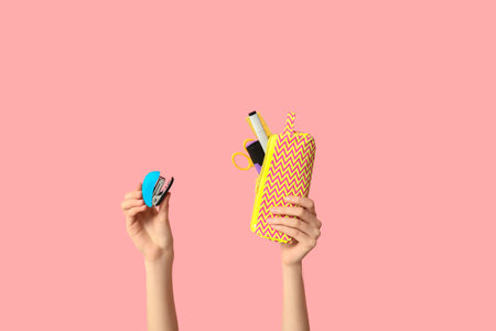 Female hands holding pencil case with stationery and stapler on pink background