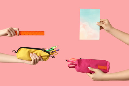 Female hands holding notebook and pencil cases with stationery on pink backgroundの写真素材