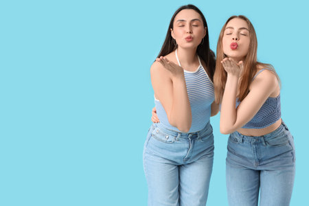 Beautiful young lesbian couple blowing kiss on blue background