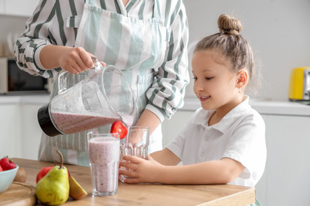 Mother and little daughter pouring smoothie into glasses in kitchenの写真素材