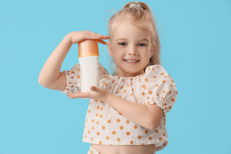 Cute little girl with sunscreen cream on blue background