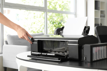 Female hands putting paper sheet in modern printer on table in stylish office