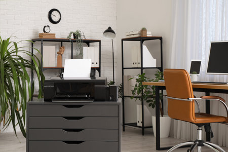 Modern printer on black chest of drawers near workplace in office