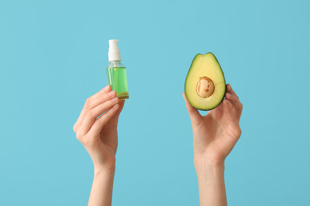 Female hands with bottle of cosmetic product and avocado on blue backgroundの写真素材