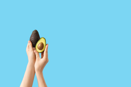 Hands holding whole and cut avocado on blue background