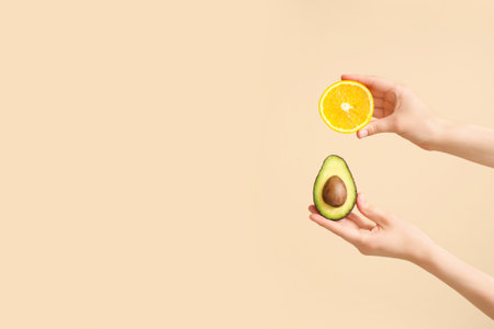 Hands holding cut avocado and orange on beige background