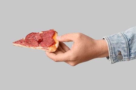 Male hand with piece of tasty pepperoni pizza on gray backgroundの写真素材