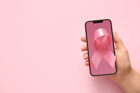 Female hand with modern mobile phone and pink ribbon on color background, closeup. Breast cancer awareness conceptの写真素材