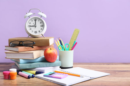 Set of different stationery with eyeglasses and alarm clock on wooden table against color wall