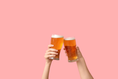 Female hands with fresh beer in pints on pink backgroundの写真素材