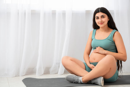 Young pregnant woman sitting on yoga mat in gymの写真素材