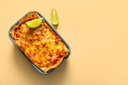 Baking dish with tasty enchilada and lime on color backgroundの写真素材