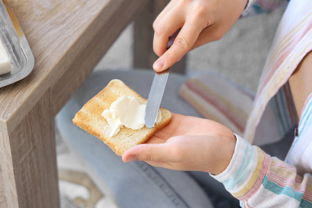 Beautiful young woman spreading tasty toast with butter at home, closeupの写真素材