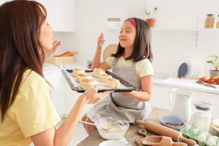 Happy Asian mother with her little daughter cooking cinnamon rolls at table in kitchenの写真素材
