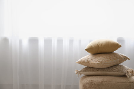 Cushions on pouf near light curtain in roomの写真素材