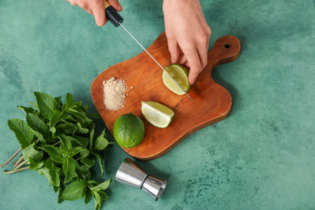 Young woman cutting lime for preparation mojito on green background
