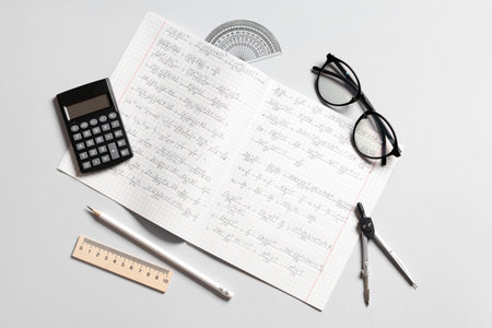 Copybook with handwritten maths formulas, eyeglasses and stationery on gray backgroundの写真素材
