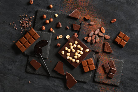 Sweet chocolate with hazelnuts, cocoa beans and powder on dark background
