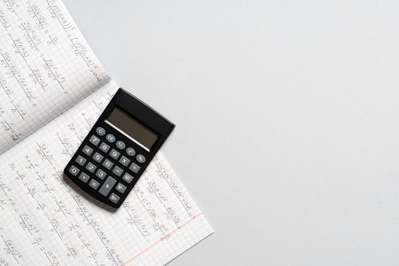 Copybook with handwritten maths formulas and calculator on gray background