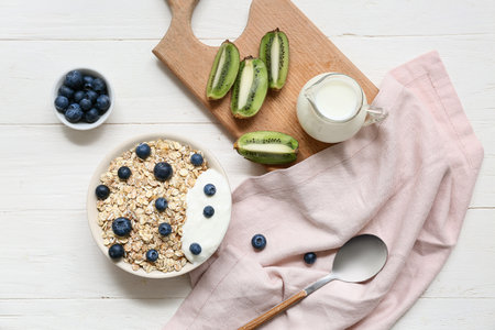 Napkin, wooden board, kiwi, bowl with raw oatmeal and berries on white wooden backgroundの写真素材