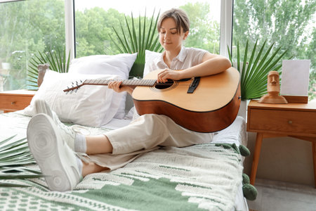 Young woman playing guitar in bedroom