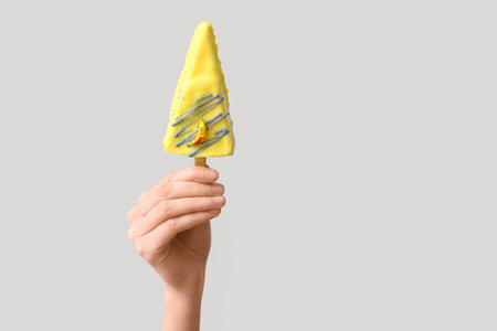 Female hand with tasty cheesecake pop on gray background