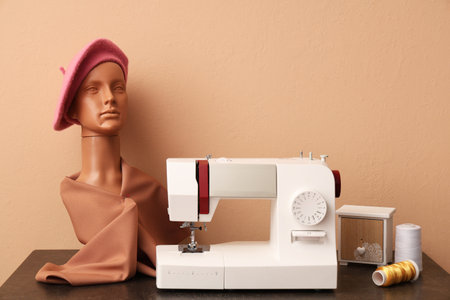 Modern sewing machine with threads and mannequin head on beige background