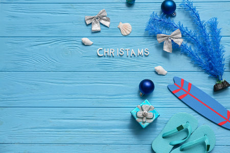 Christmas decor, kid's flip-flops, toy surfboard and word CHRISTMAS on blue background. Top view