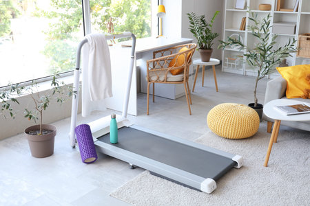 Treadmill with towel, water bottle and foam roller in living room interior