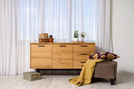 Wooden cabinet with houseplants, decor and ottoman near window