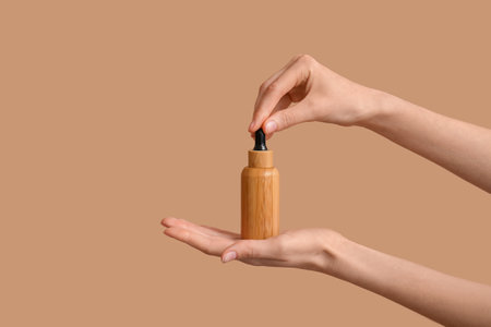 Female hands with bottle of cosmetic product on brown backgroundの写真素材