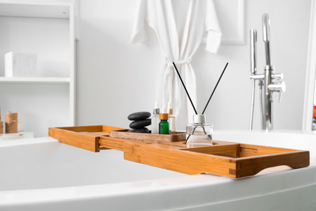 Wooden tray with aroma diffuser and bottles of essential oil on bathtub in bathroomの写真素材
